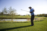A golfer in mid-swing, focusing on hitting a perfect shot under a clear blue sky on a premium golf course.